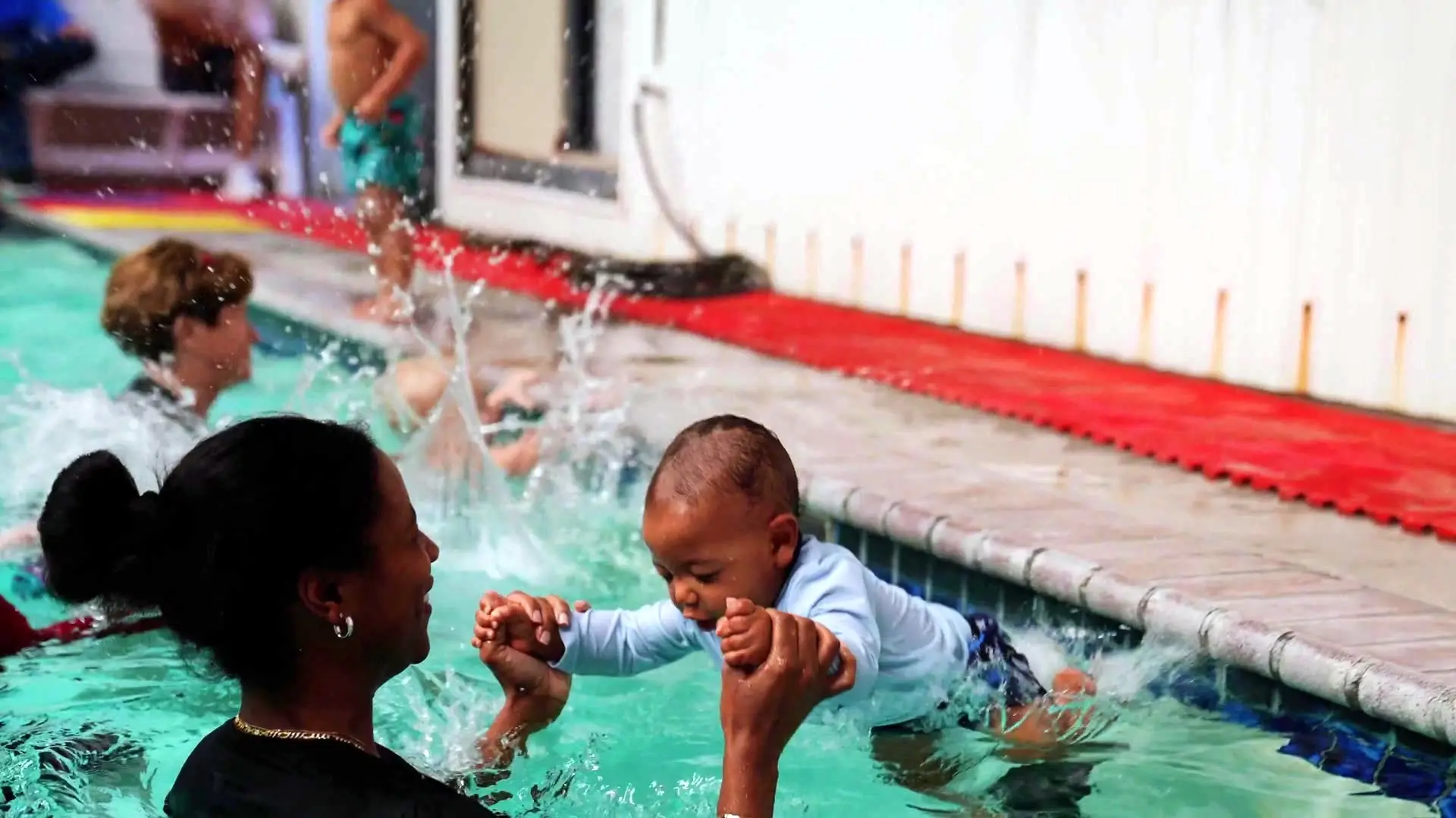 An instructor catches a toddler jumping into the pool during a summer session
